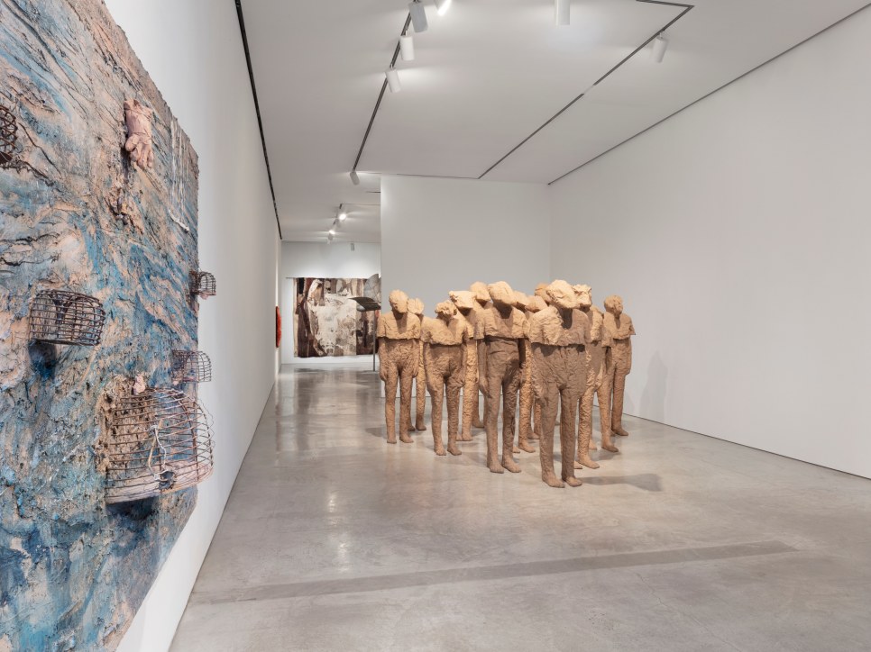 Installation view of large scale textured canvas with birdcages by Anselm Kiefer and group of multiple burlap and resin life-size standing figures with different heads by Magdalena Abakanowicz along with her textiles and a steel bird sculpture