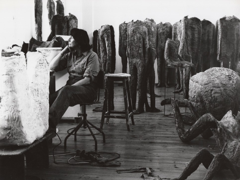 Black and white photographic portrait of Magdalena Abakanowicz in her studio surrounded by sculptures