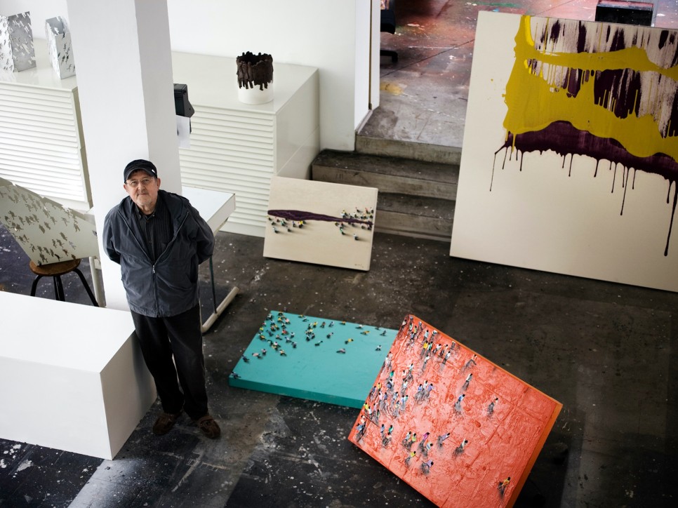 Color photographic portrait of Juan Genovés in his studio surrounded by paintings