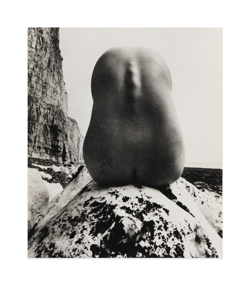 Black and white photograph by Bill Brandt showing the nude back of a figure atop a rock on the beach 