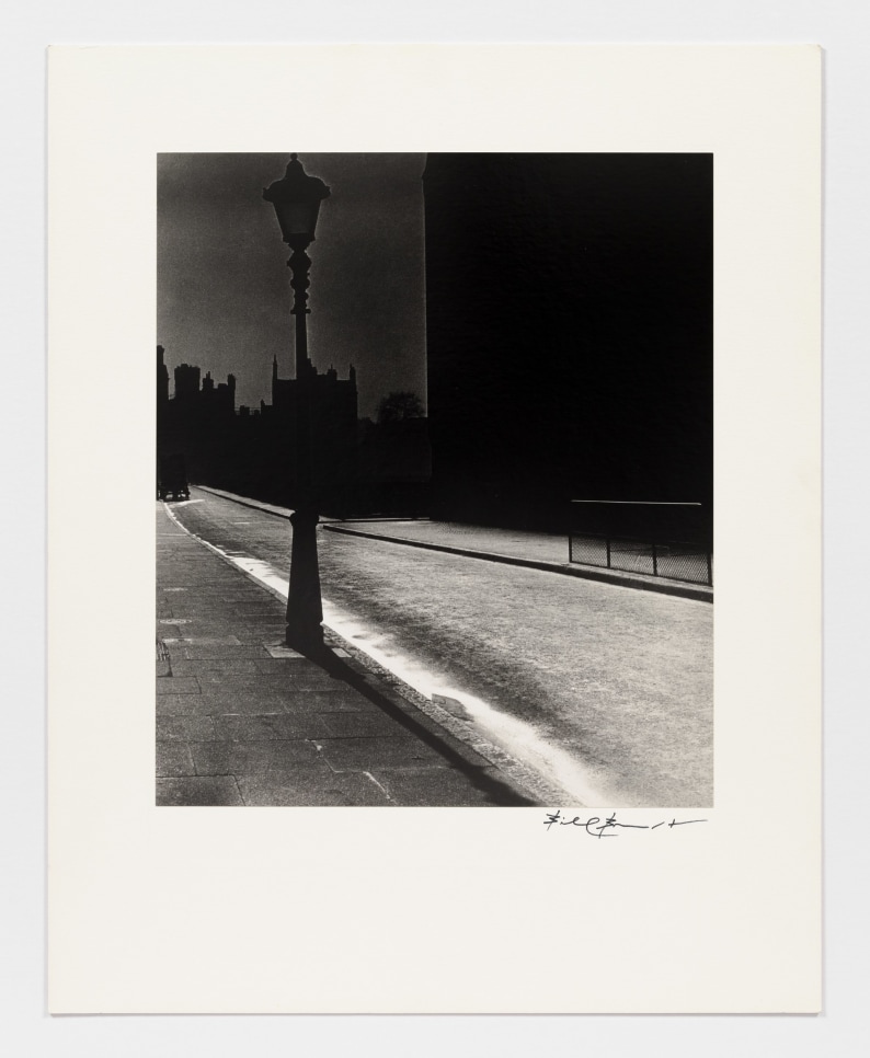 Black and white photographic by Bill Brandt featuring an empty street at night and the silhouette of a street lamp