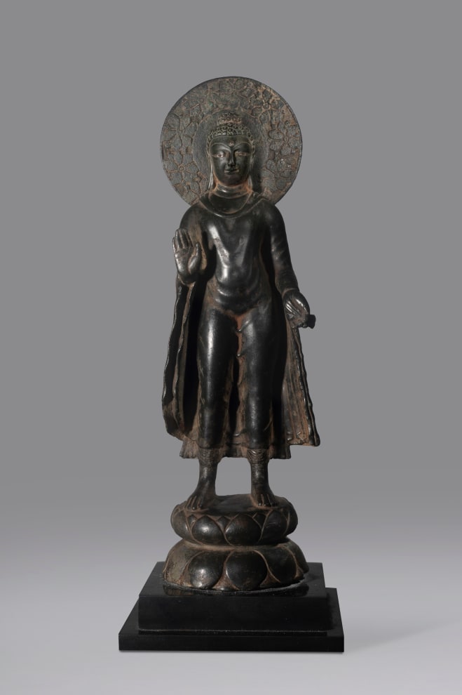 The Buddha Sakyamuni stands on a pedestal composed of two convex sections