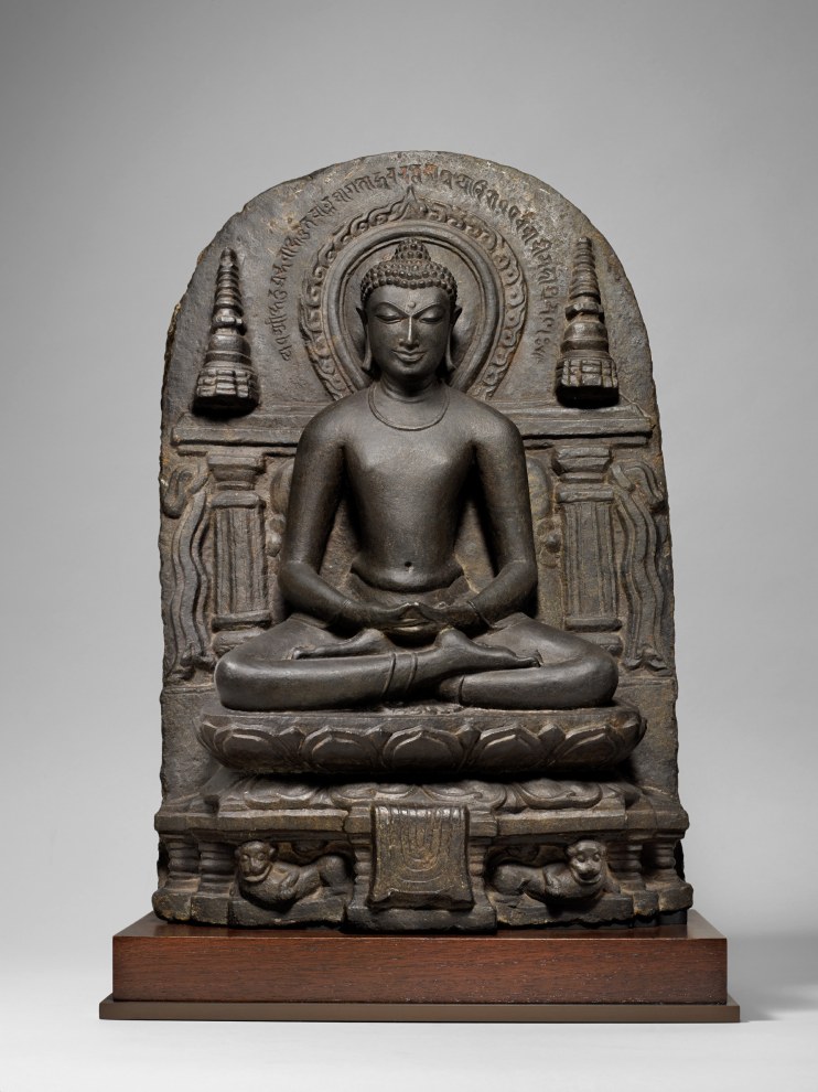 In this elegant and serene stele, the central figure of Buddha is flanked by two cylindrical stupas and is seated atop a lotus pedestal that in turn rests upon a lion throne.