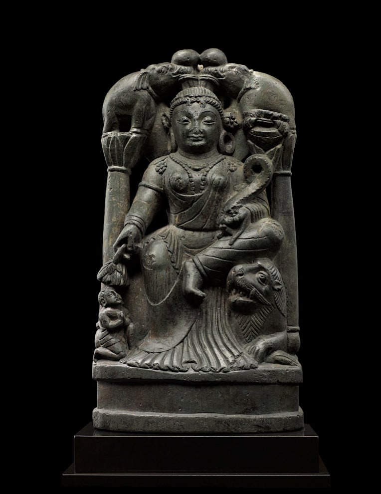 Sculpture of Gaja Lakshmi, the Goddess of Fortune, who is venerated as a bringer of good fortune and well-being to the earth, of which she was an early personification.  She wears a long transparent chiton with delicate pleats pooling on the base, beaded jewelry, large hoop earrings, and stylized mural crown. 